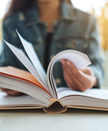 SSZ Beratung Bücher & Lektüre Person in Jeansjacke blättert in einem aufgeschlagenen Buch.