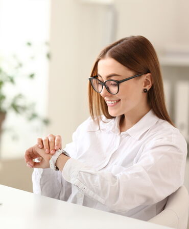 Frau mit Brille schaut lächelnd auf ihre Armbanduhr.